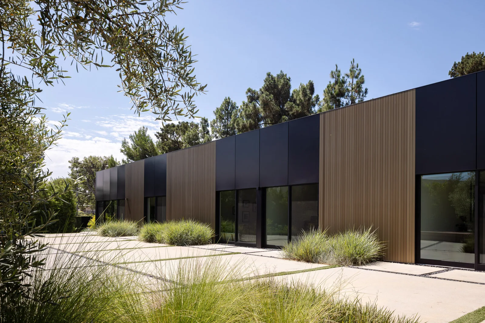 Bronze and Black House features vertical wood panels and black metal cladding with large horizontal windows and landscaped garden areas.