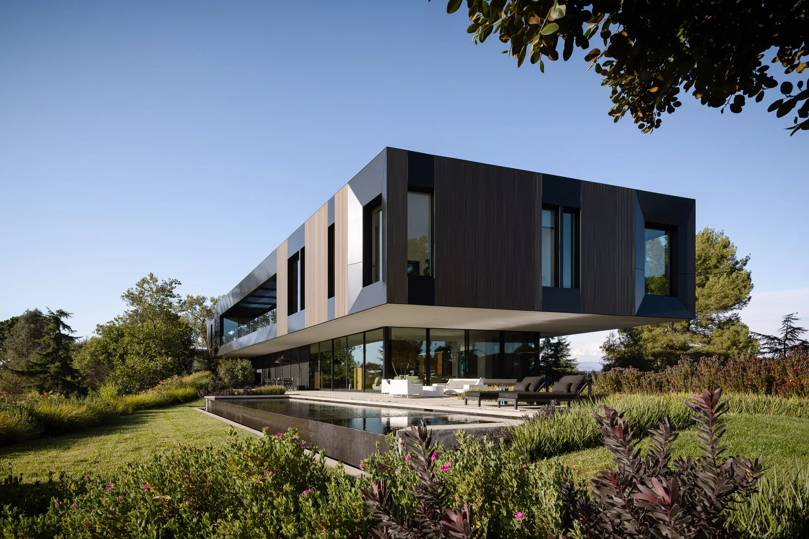 The Bronze and Black House by SPF:architects features a cantilevered upper floor with vertical wood panels and extensive glazing with mountain views.