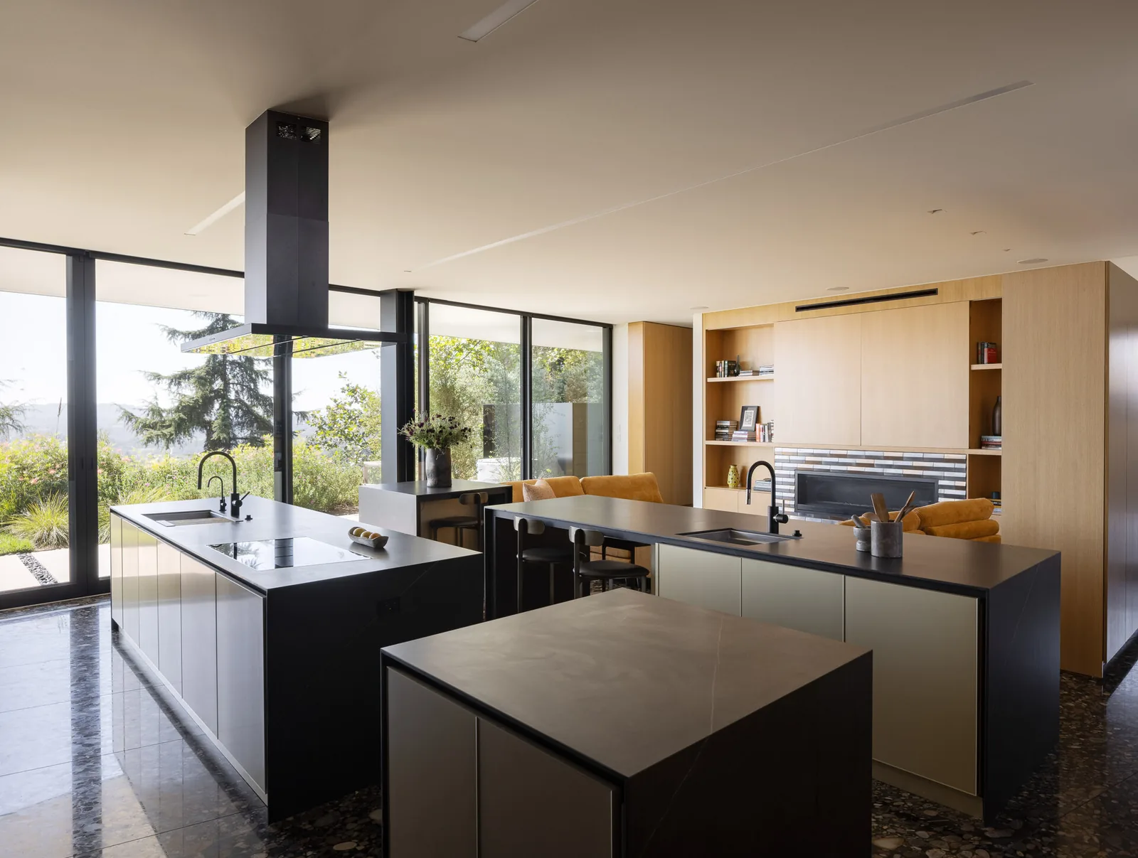 Kitchen featuring black countertops, wood-paneled walls, and expansive floor-to-ceiling glazing with views of landscaped greenery.