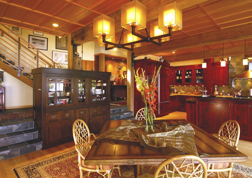 Dining area and kitchen interior featuring rich wood cabinetry and a large chandelier lighting the space.