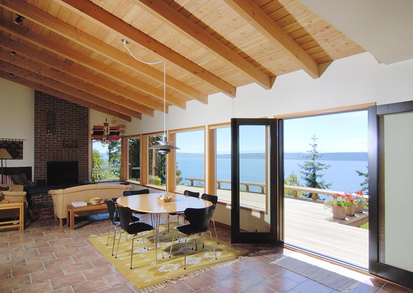 Dining room with vaulted wood ceiling and folding glass doors opening to an outdoor deck with water views.