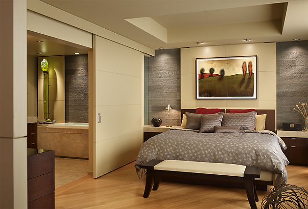 Bedroom with wood flooring, fabric bedding, framed artwork, and a connected bathroom through sliding doors.
