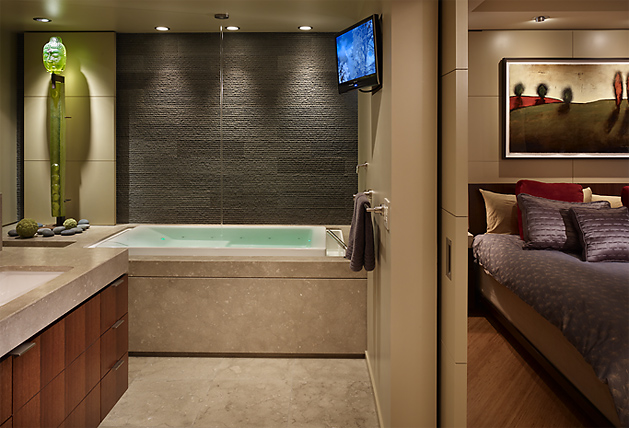 The Watermark Tower bathroom features a built-in tub with textured wall tile and wood cabinetry, adjacent to a bedroom with contemporary decor.