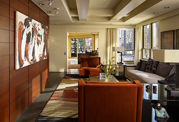 Living room in Watermark Tower Condominium features wood paneling, abstract art, and city skyline views through large windows.
