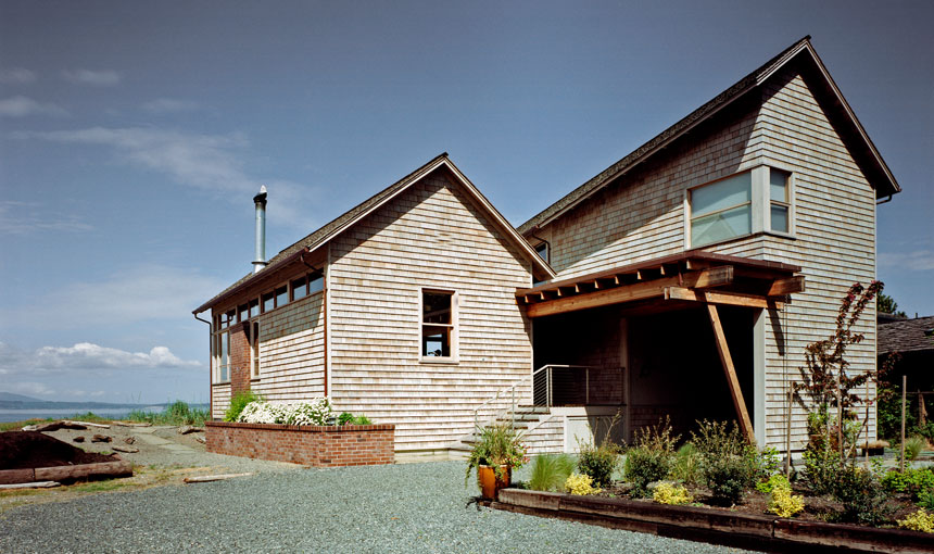 Exterior view of a two-story townhouse with wood shingle siding and a covered entry porch under a gable roof.
