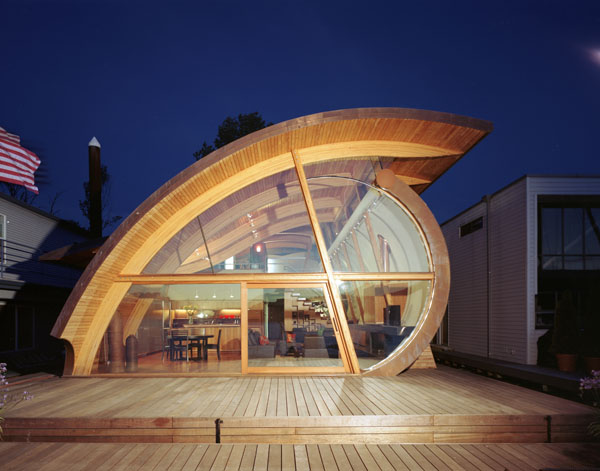 Night view of the Fennel Residence showing a curved wooden and glass facade with an open interior and wooden deck in front.