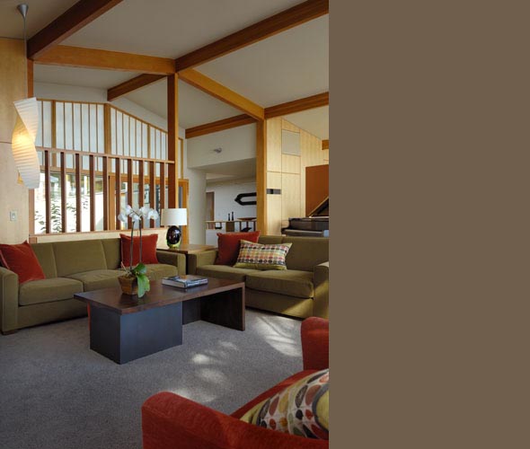 A midcentury living room with olive green sofas, wooden beams on the ceiling, and a dark wood coffee table.