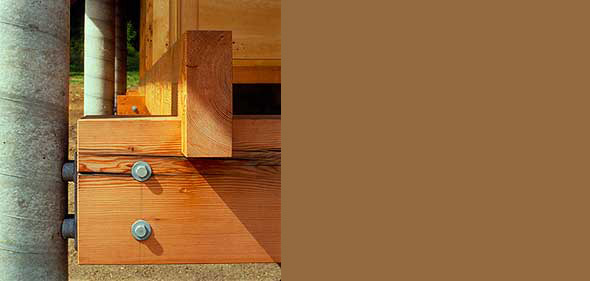 Close-up view of a timber frame corner joint with metal bolts.