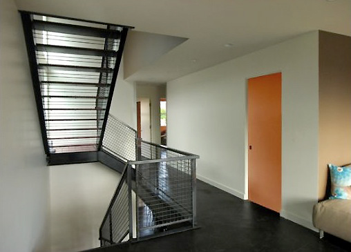 Interior hallway with black metal stair railing and an orange door on the right side.