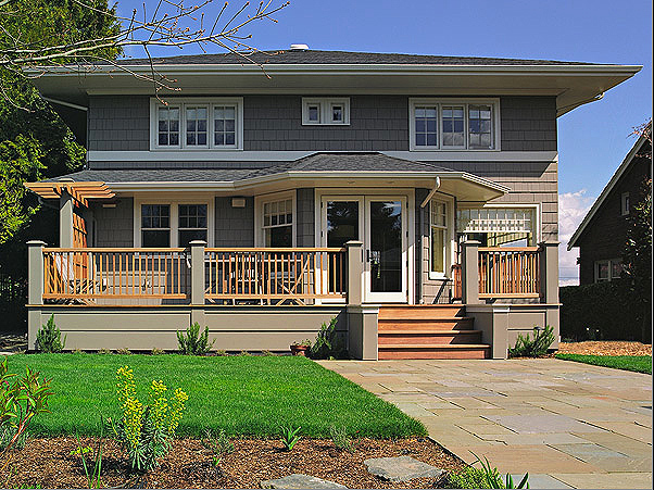 Rear exterior view of a two-story house with a raised wooden deck and landscaping in the foreground.