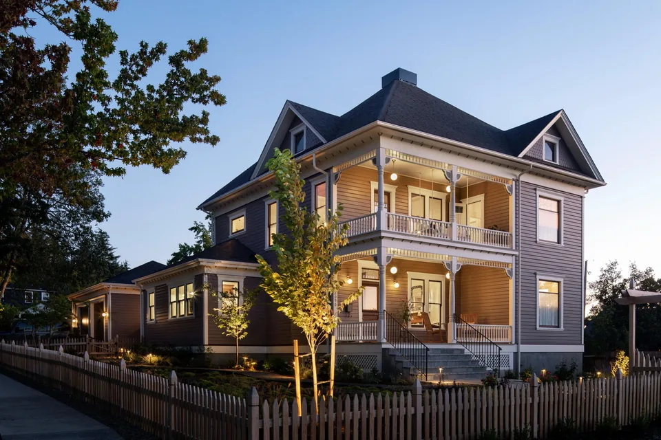 Two-story Queen Anne style house with gable roof and wrap-around porch lit at dusk