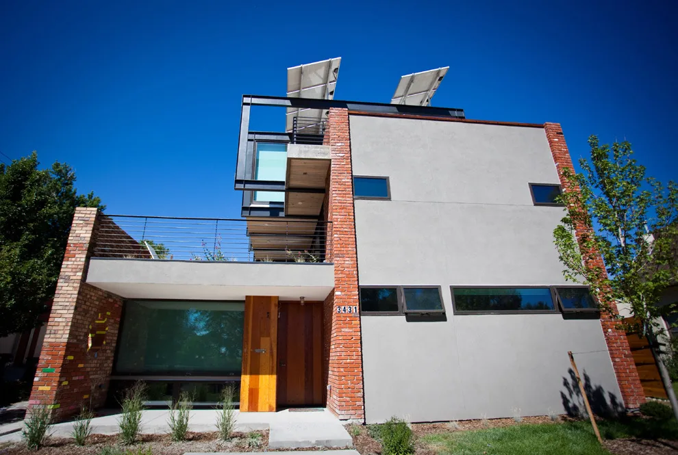 Modern multi-story house with concrete and brick exterior, horizontal narrow windows, and solar panels on the flat roof under a clear blue