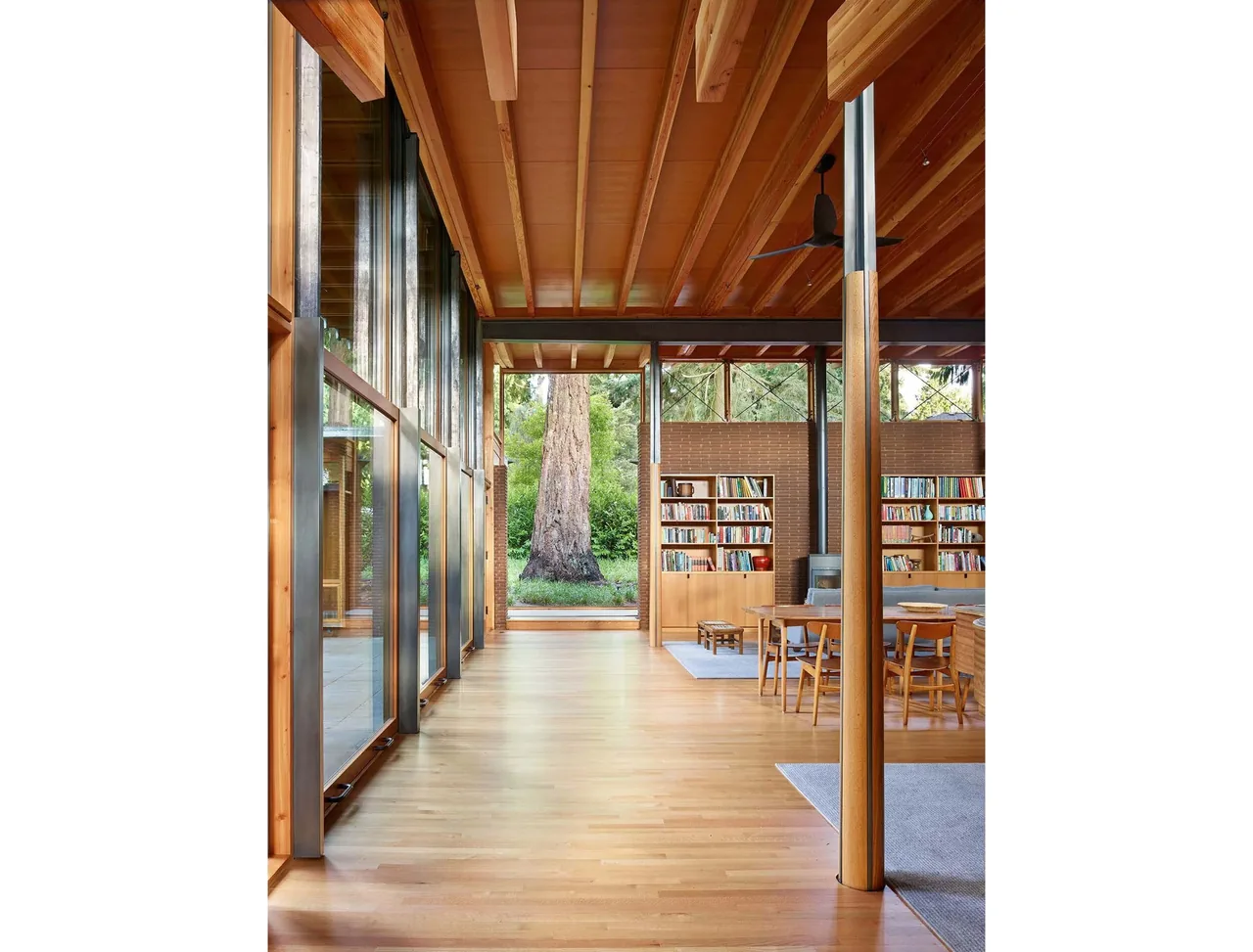 Interior view of a living and dining area with exposed wooden ceiling beams, large metal framed windows, and wooden floors.