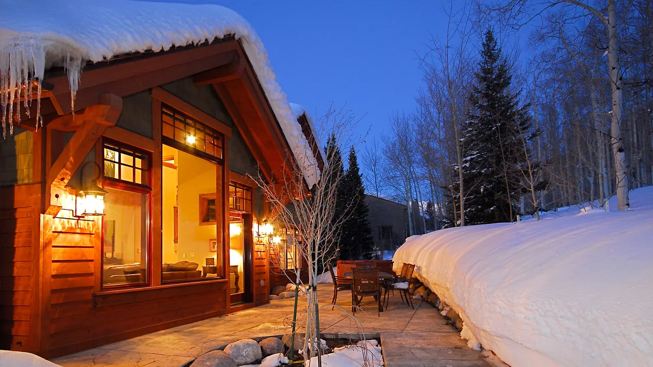 Wooden exterior of a house with snow-covered roof and patio at dusk with outdoor furniture.