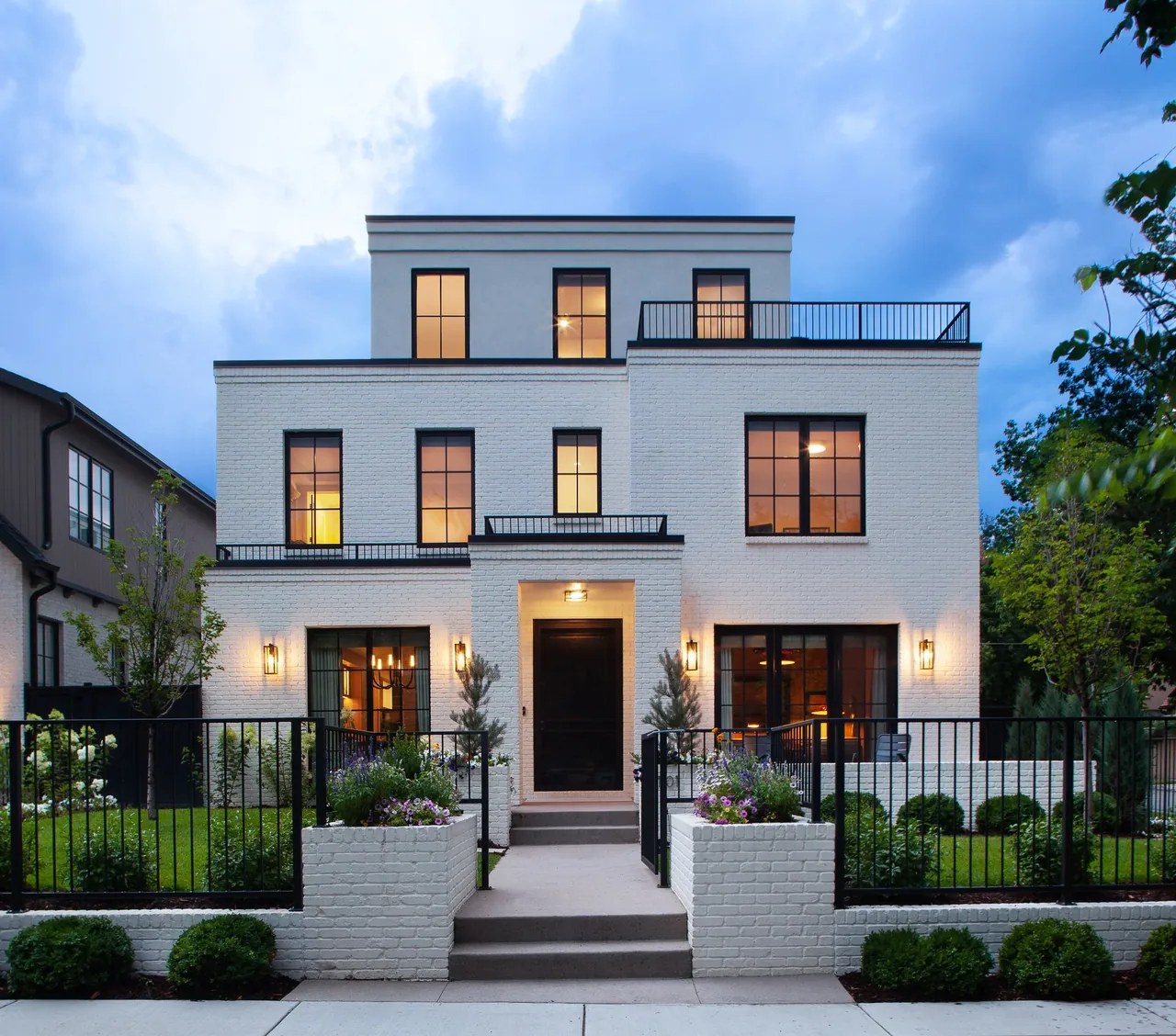 Three-story white painted brick house with black framed windows and black metal railings at dusk.