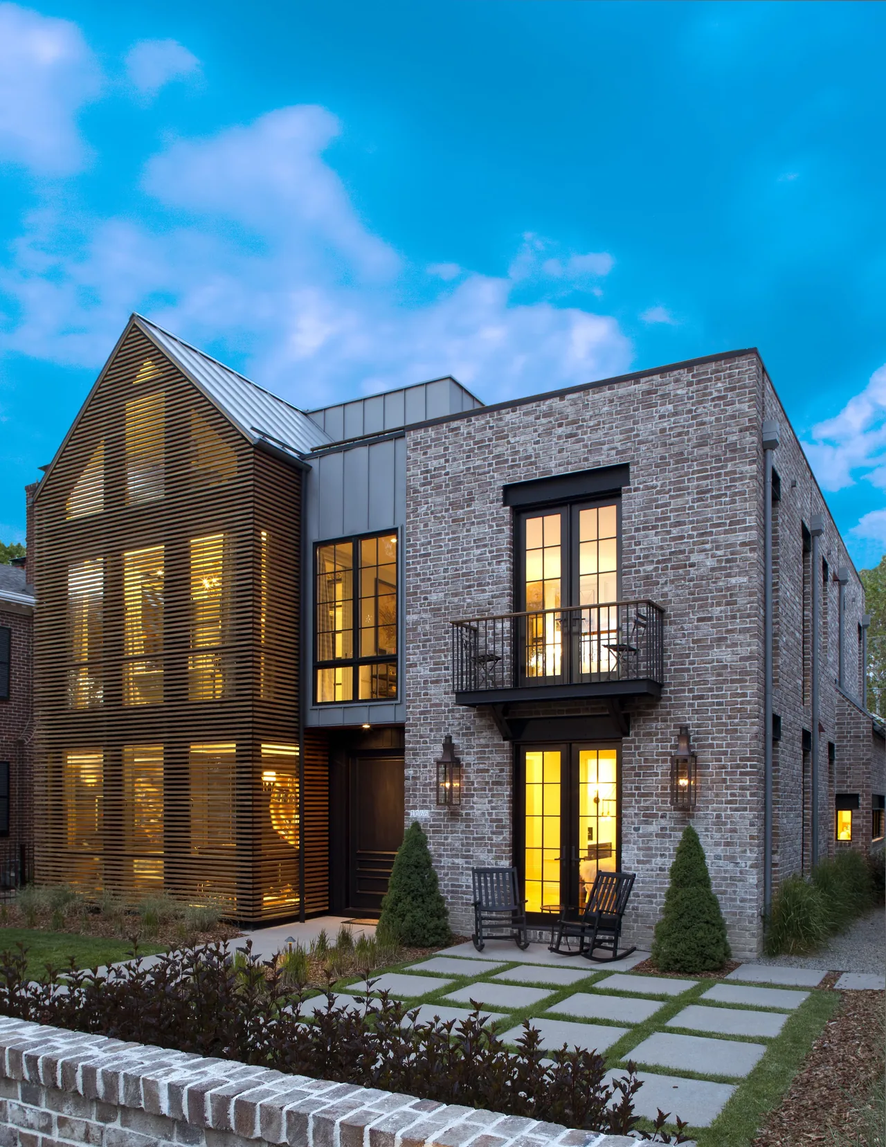 Two-story modern house with a brick facade and a wooden slatted gable section at dusk.