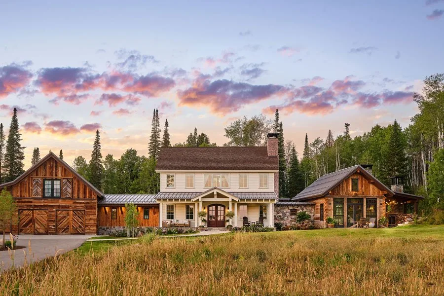 Front exterior view of a large farmhouse-style home with multiple gable roofs and wooden garage doors at sunset.