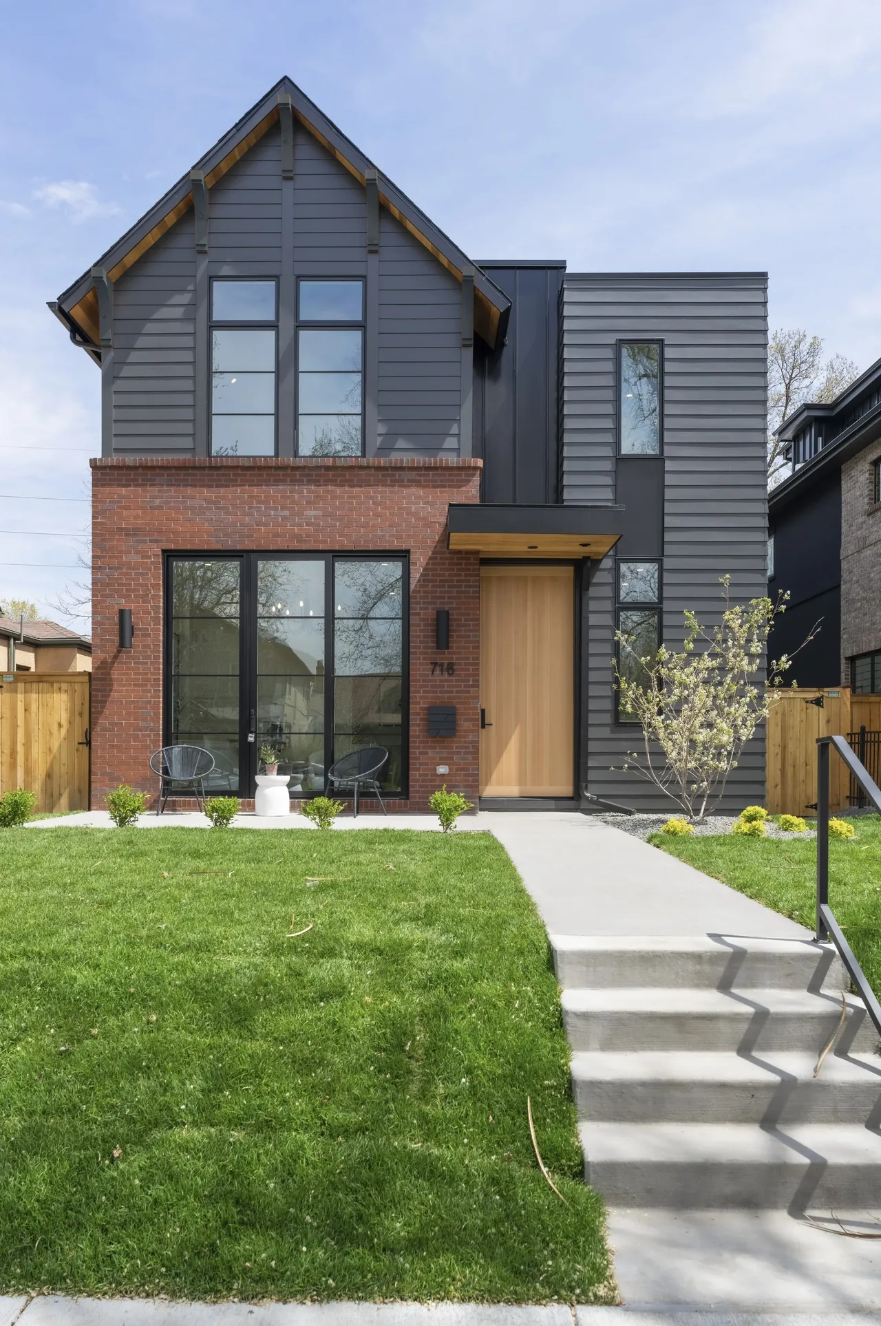 Front exterior view of a modern two-story house with a brick and gray siding facade and large black-framed windows.