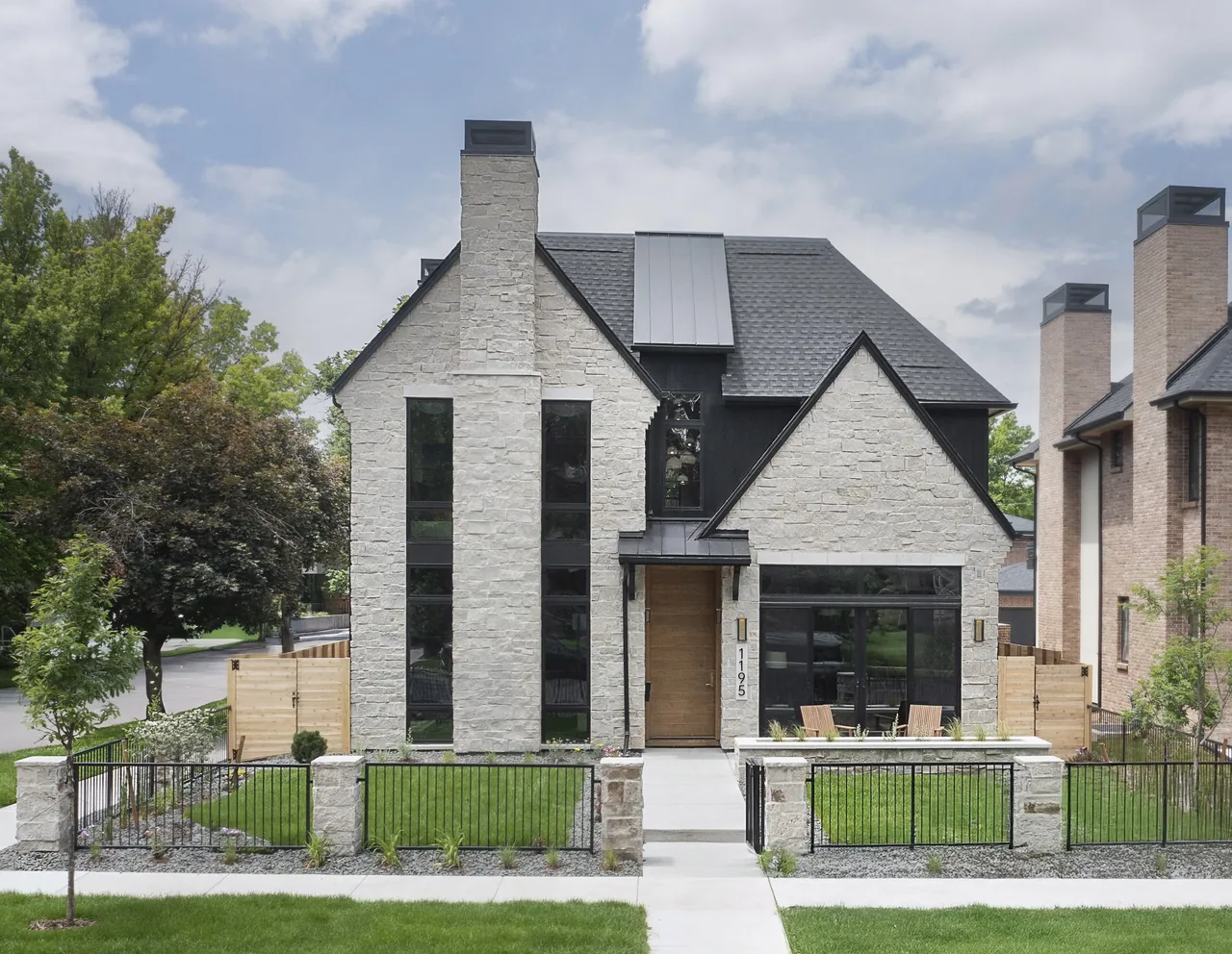 Front exterior view of a modern two-story house with light stone facade, steep dark shingle roof, tall vertical windows, and a central light