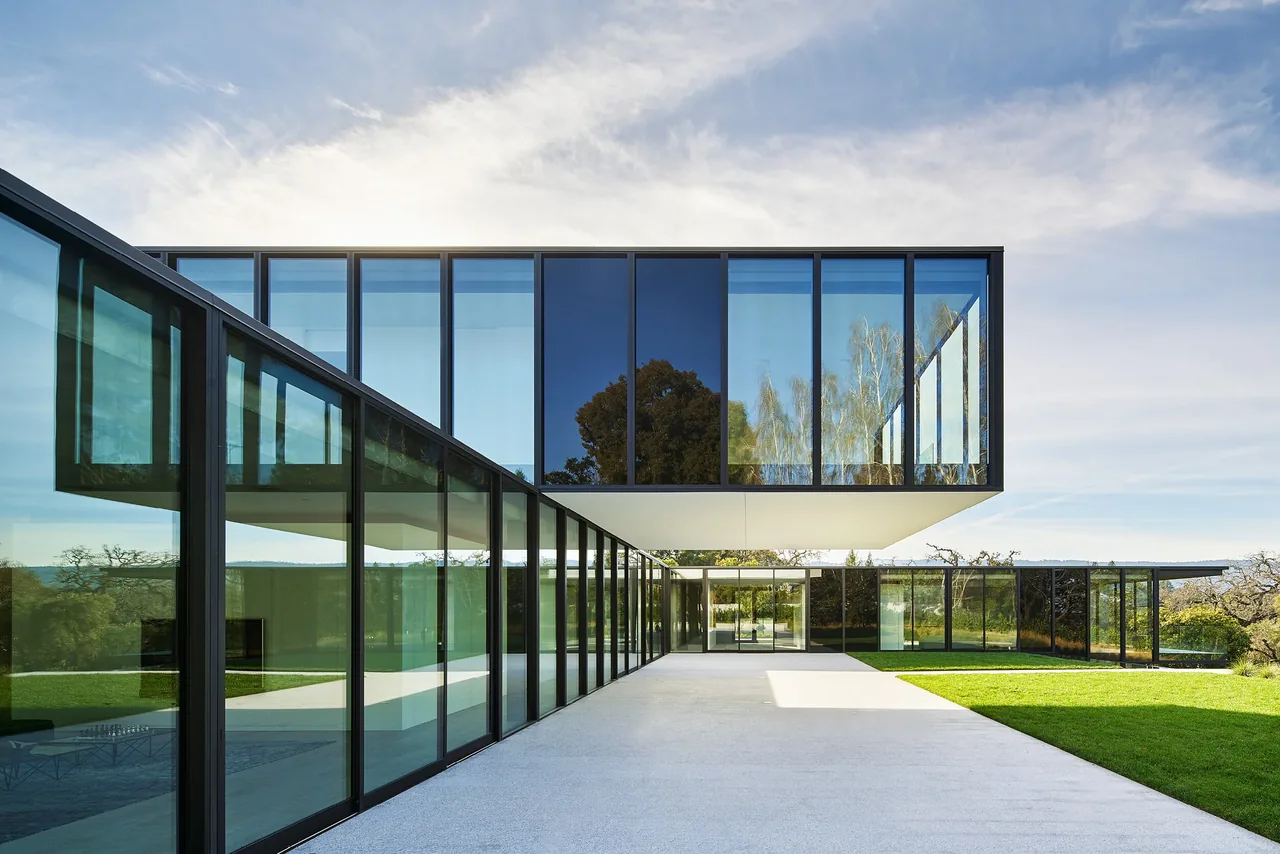Modern house with a large cantilevered second floor and extensive floor-to-ceiling glass walls on the ground floor.
