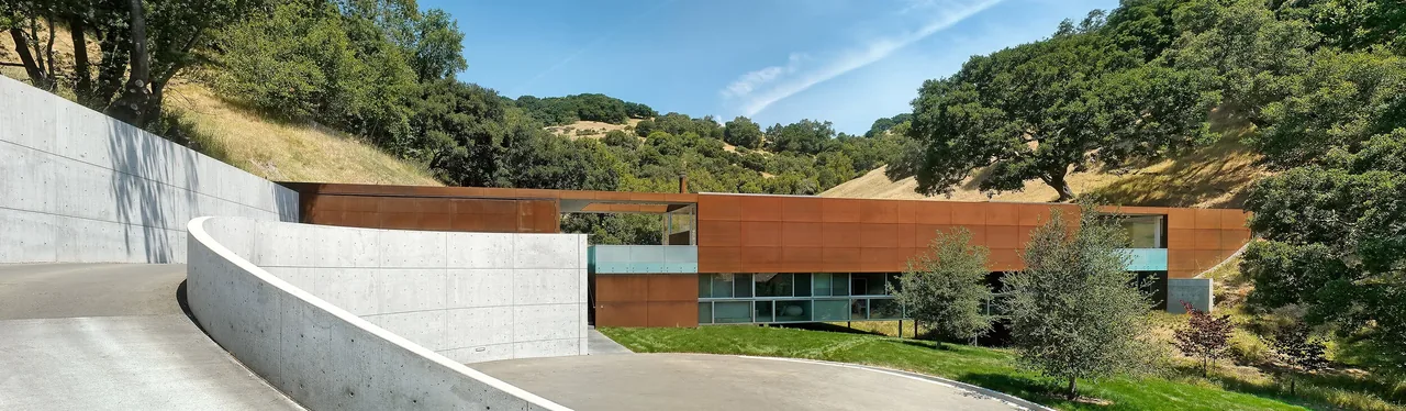 Modern concrete and steel house built into a grassy hillside under a blue sky.