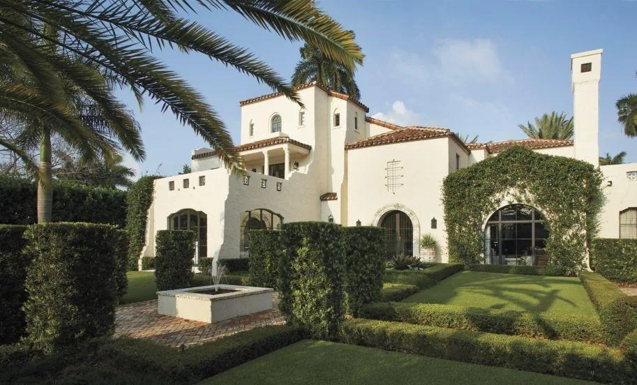 Exterior view of Venetian Island Residence with stucco walls, red tile roof, and manicured hedges under palm trees.