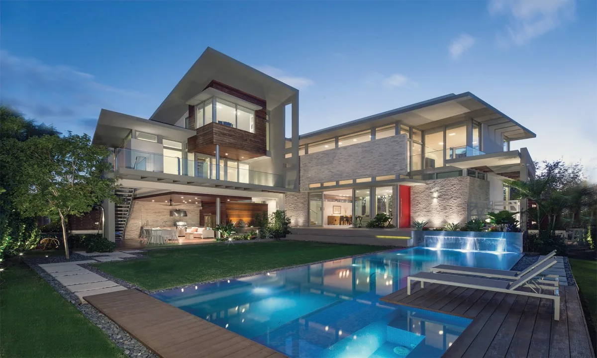 Modern multi-level house with illuminated pool and waterfall feature at dusk.