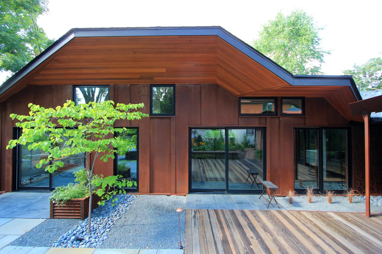 Exterior of a modern house with rust-colored metal siding and wood soffits above large black-framed sliding glass doors and windows.