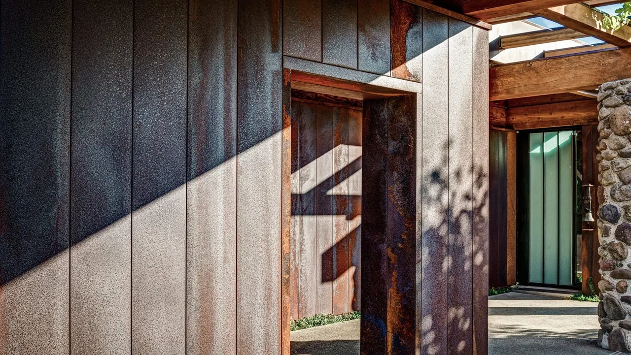 Rustic exterior doorway with metal paneling and wood beams casting shadows in sunlight.