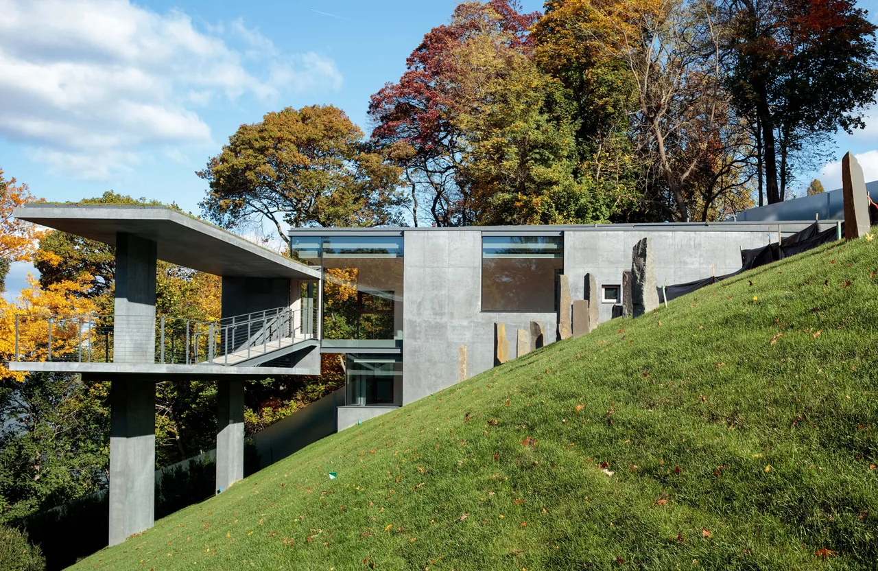 Modern concrete house on a grassy slope with large windows and a cantilevered balcony.