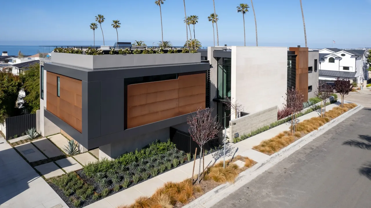 Modern two-story home with flat roof, large rectangular volumes, and landscaped front yard on a coastal street.