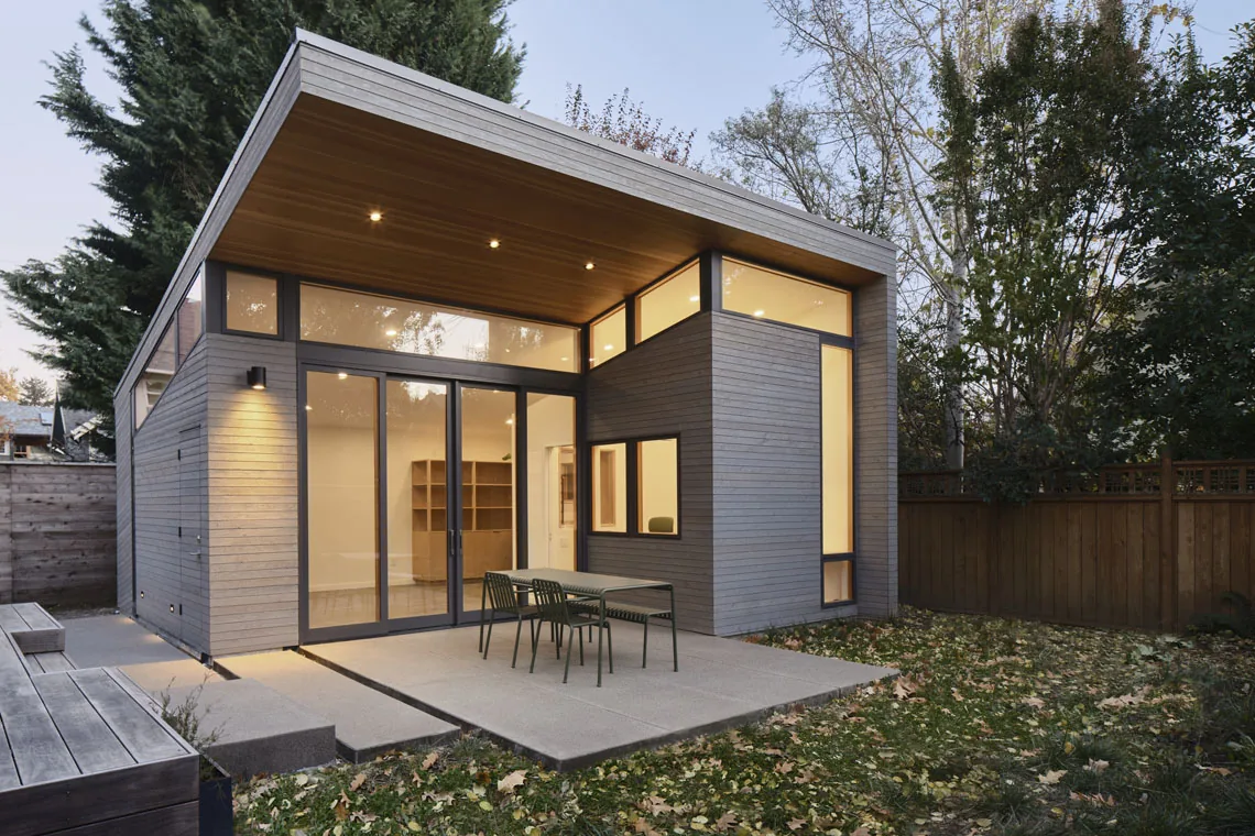 Modern single-story home with overhanging flat roof, wood siding exterior, and large glass doors opening to a concrete patio with metal-fram