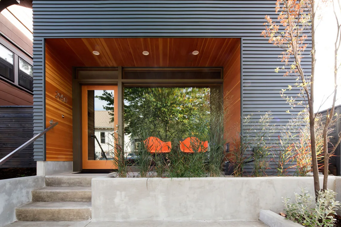 Front exterior view of an ADU with wood-paneled entry and large glass window next to an orange door.
