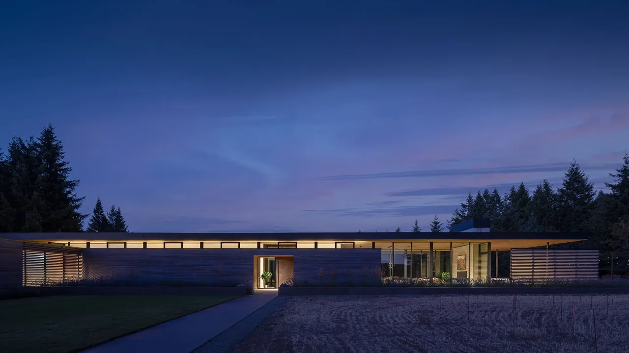 Evening exterior front view of a modern flat roof house with illuminated clerestory windows at dusk.