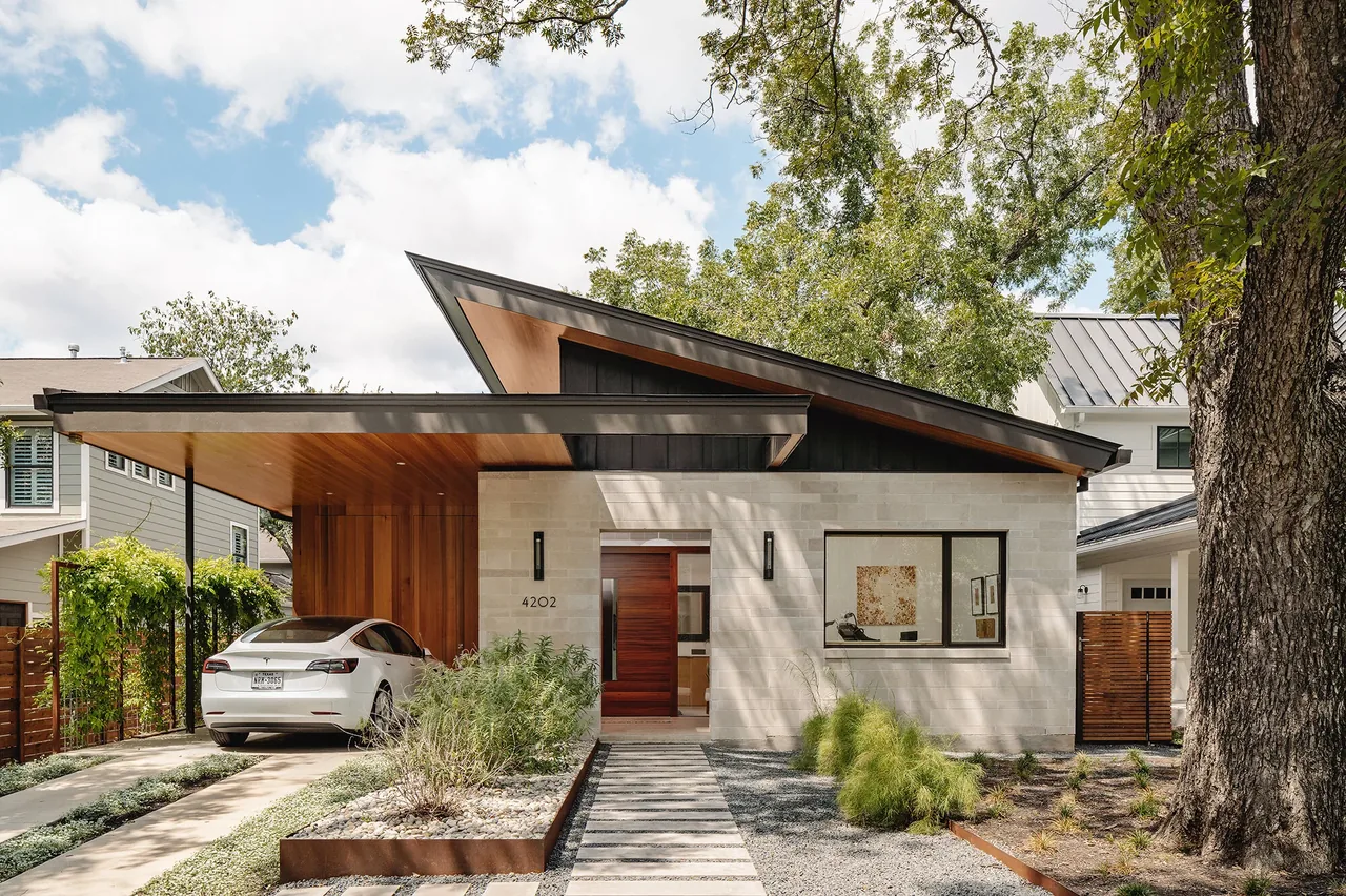 Front exterior of a modern home with a sloped roof, wood and stone walls, and carport with a white car.
