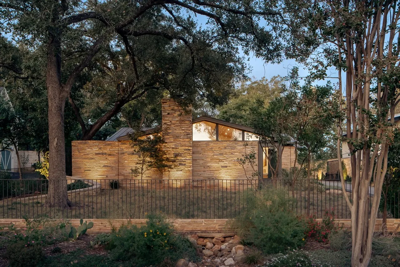 Single-story stone house with a sloped roof surrounded by trees at dusk.