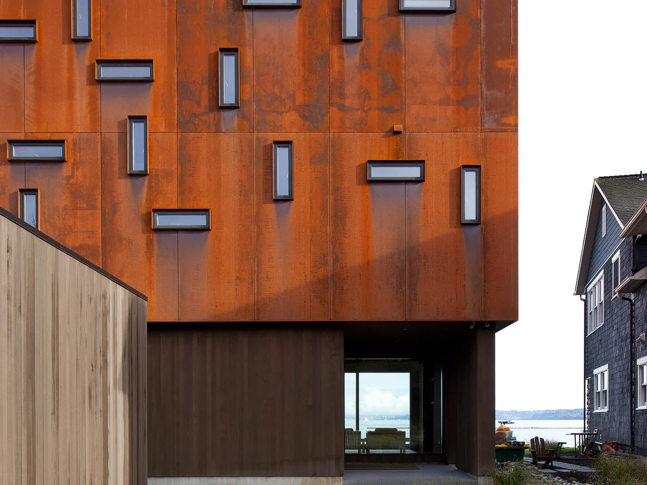 Exterior view of a modern house facade with rust-colored metal cladding and small rectangular windows.