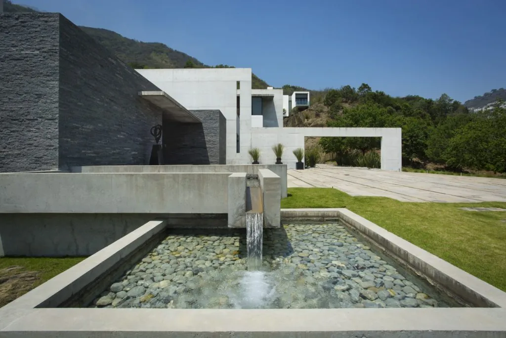 Modern house exterior with a stone water feature and concrete walls under clear blue sky.