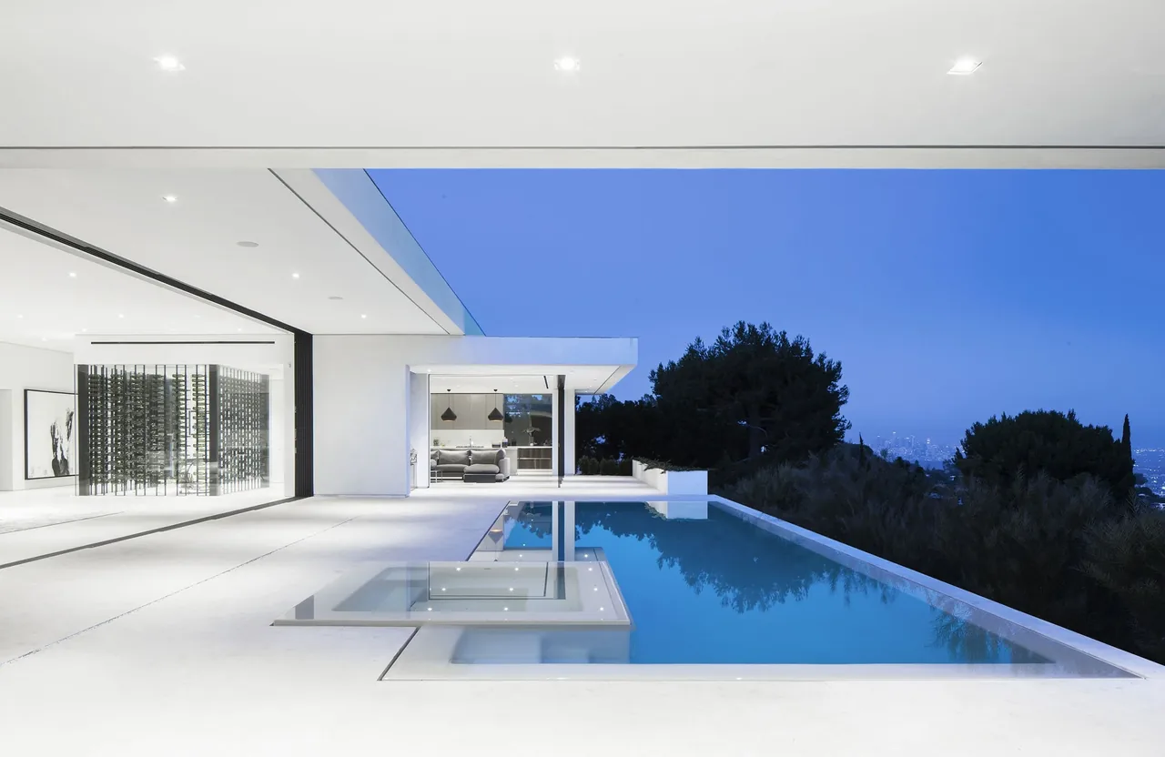 Modern poolside patio with infinity edge pool and open view of outdoor seating area at dusk.
