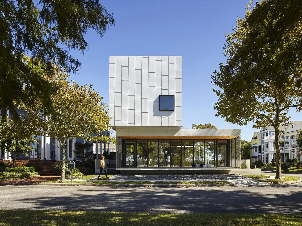 Modern cubic two-story house with a cantilevered upper level clad in metal panels and large glass windows below.