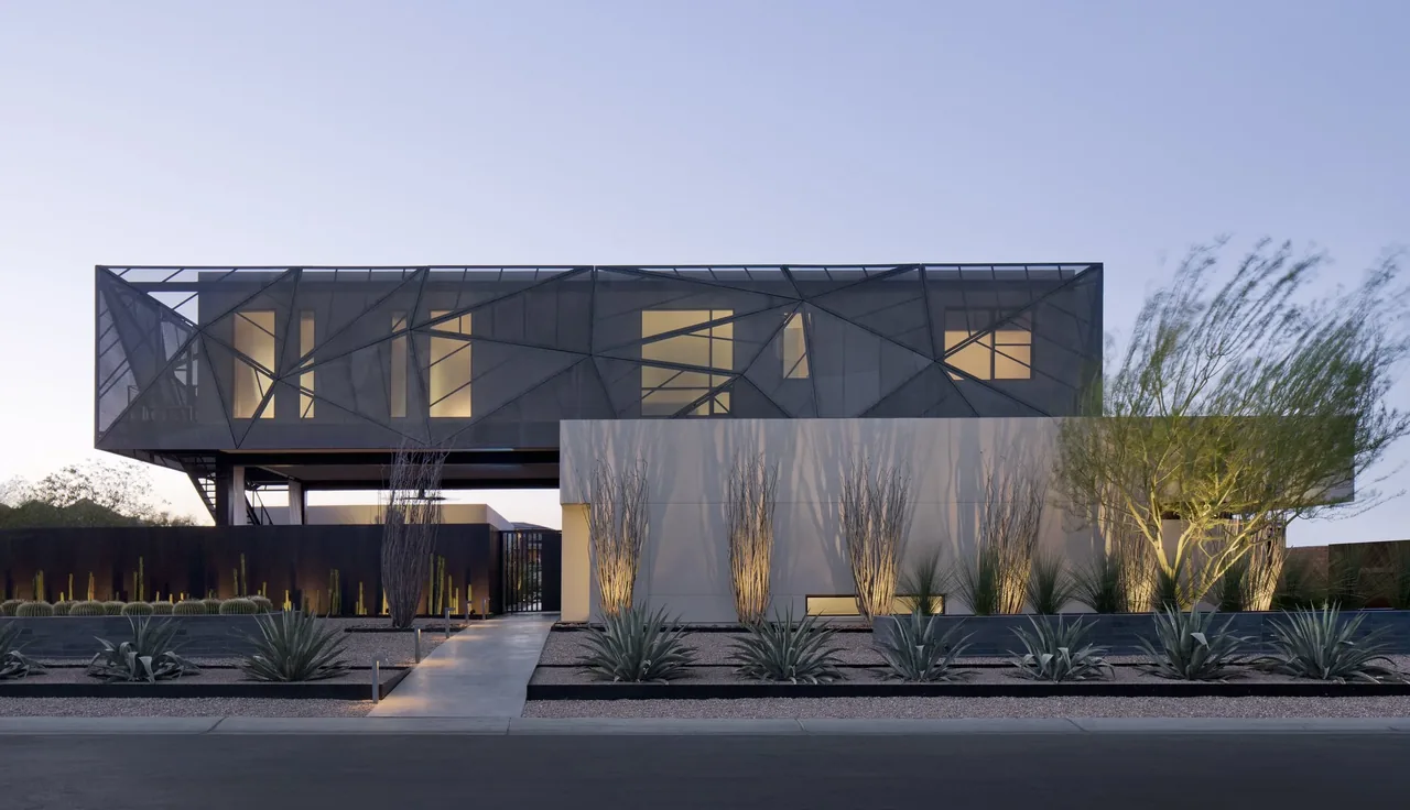 Contemporary two-story house with a geometric metal upper facade and minimalist landscaping at dusk.