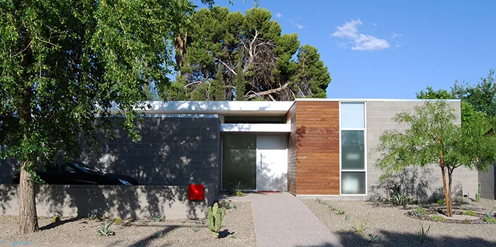 Single-story modern house front with concrete and wood facade and a glass front door under a flat roof.