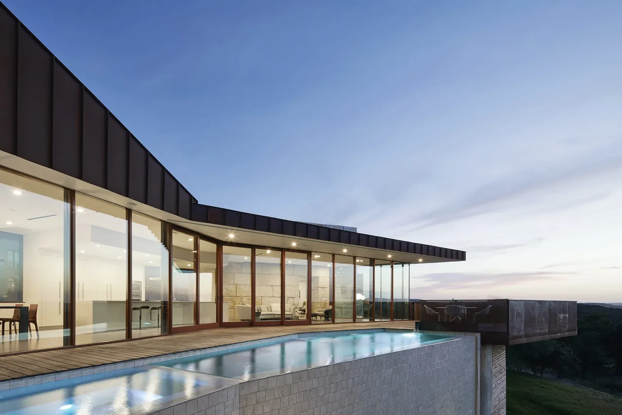 Modern house with floor-to-ceiling glass walls overlooking an infinity pool at dusk.