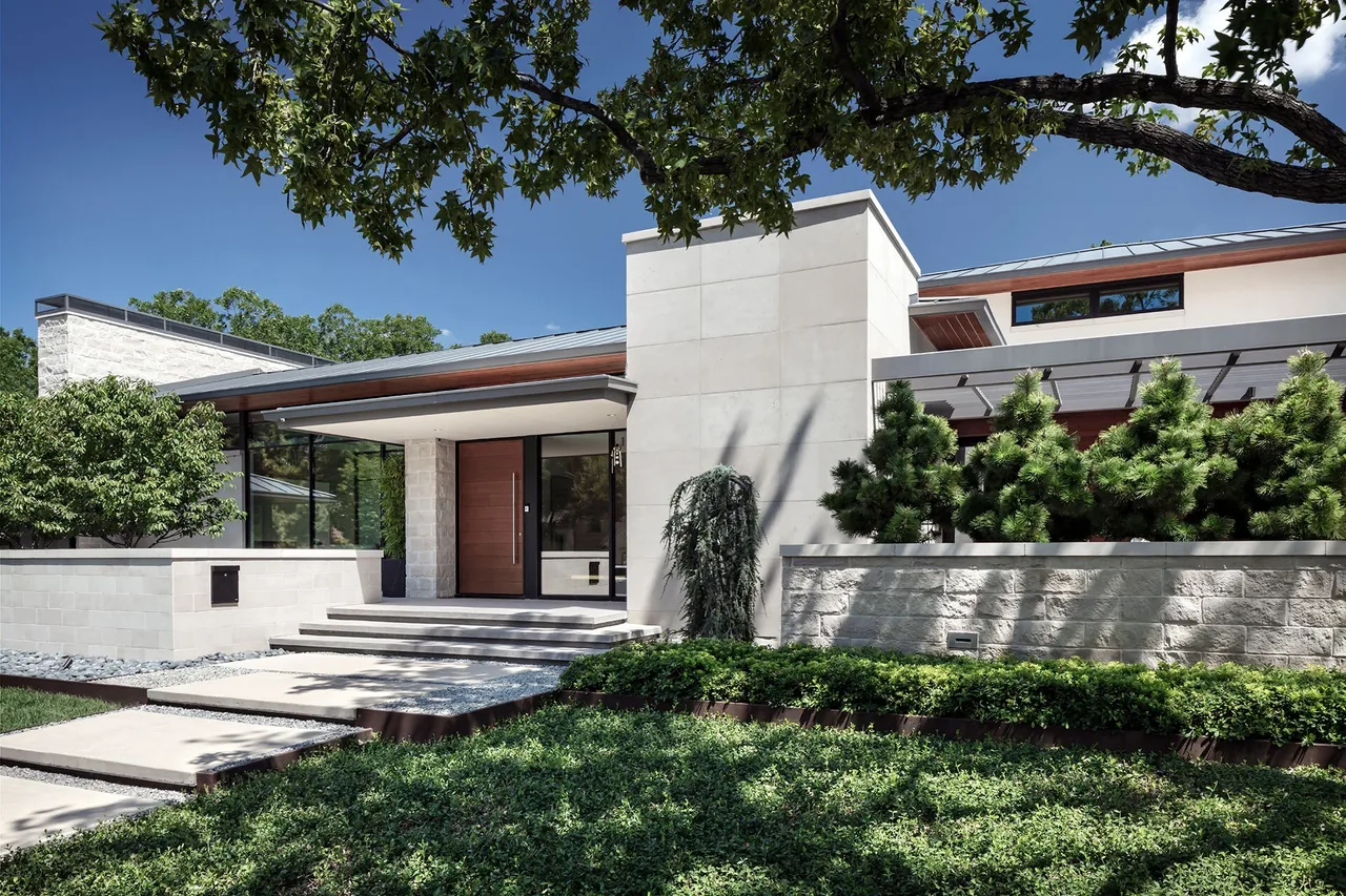 Modern house front entrance with stone steps, flat roof, and landscaped garden under a tree.