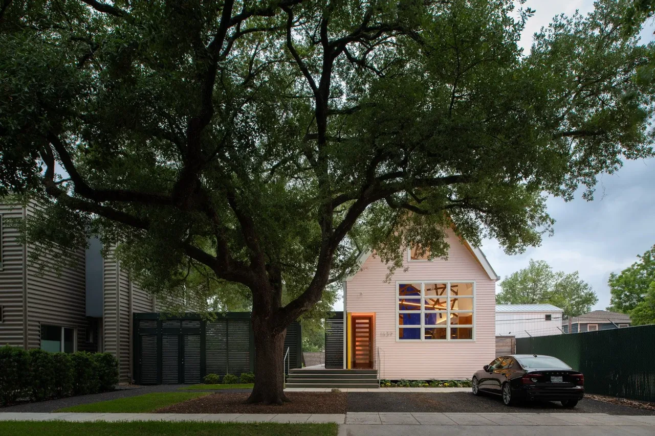 Exterior front view of a pink gable-roofed house with large windows and a tree in the front yard.