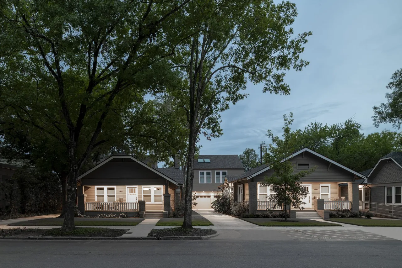 Two single-story craftsman-style houses with front porches at dusk flanking a two-story garage structure with skylights.