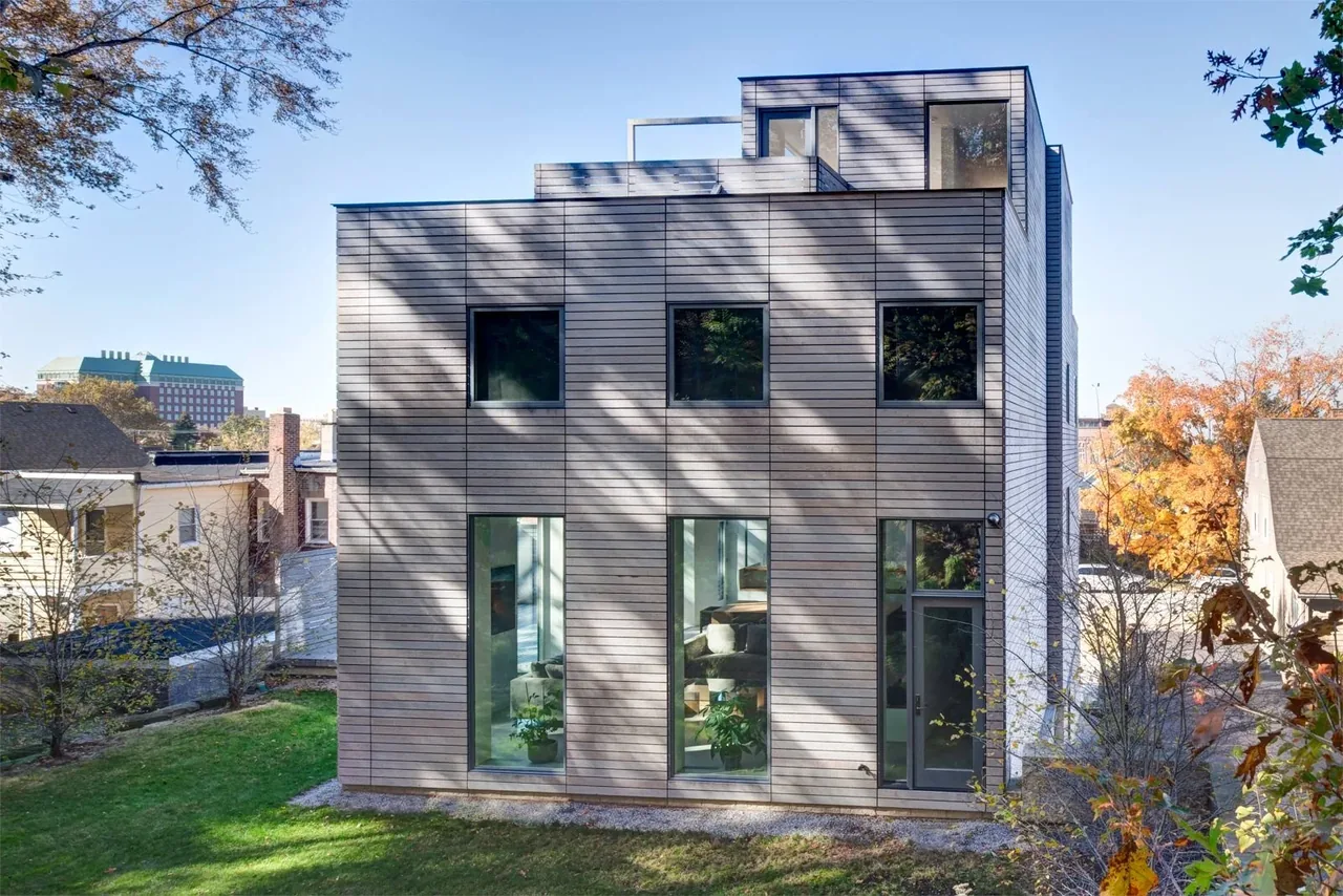 Exterior view of a modern townhouse with horizontal wood siding and multiple large windows under a clear sky.