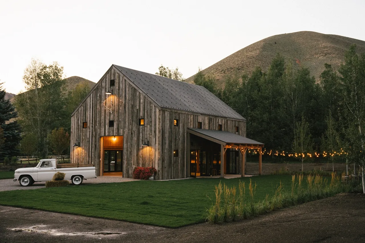 Two-story barn-style house with weathered wood siding and warm outdoor lighting at dusk.