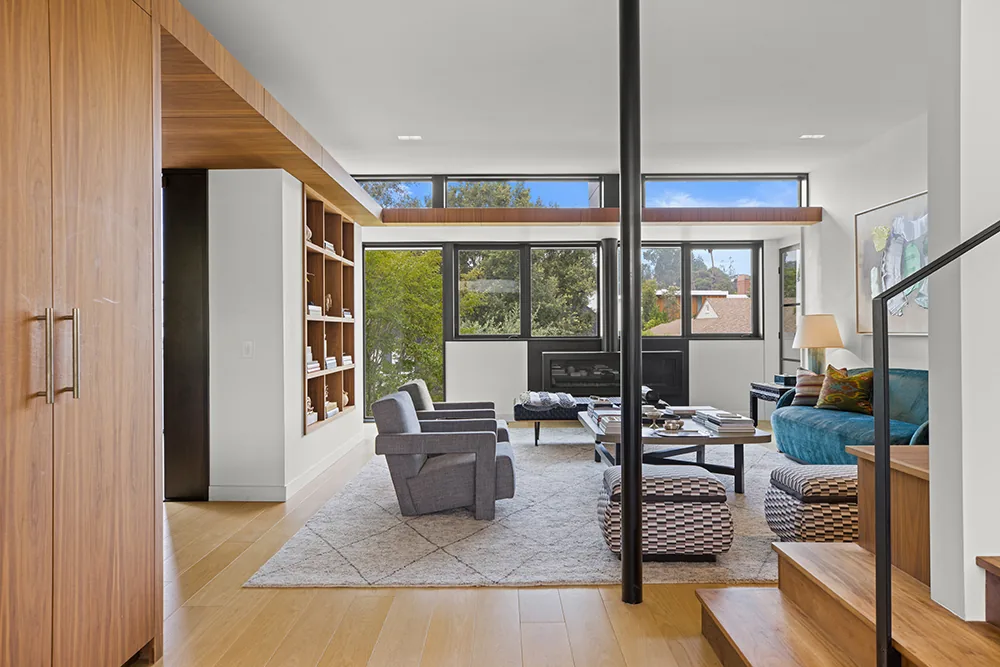 Living room with floor-to-ceiling windows and black-framed fireplace wall under clerestory windows.