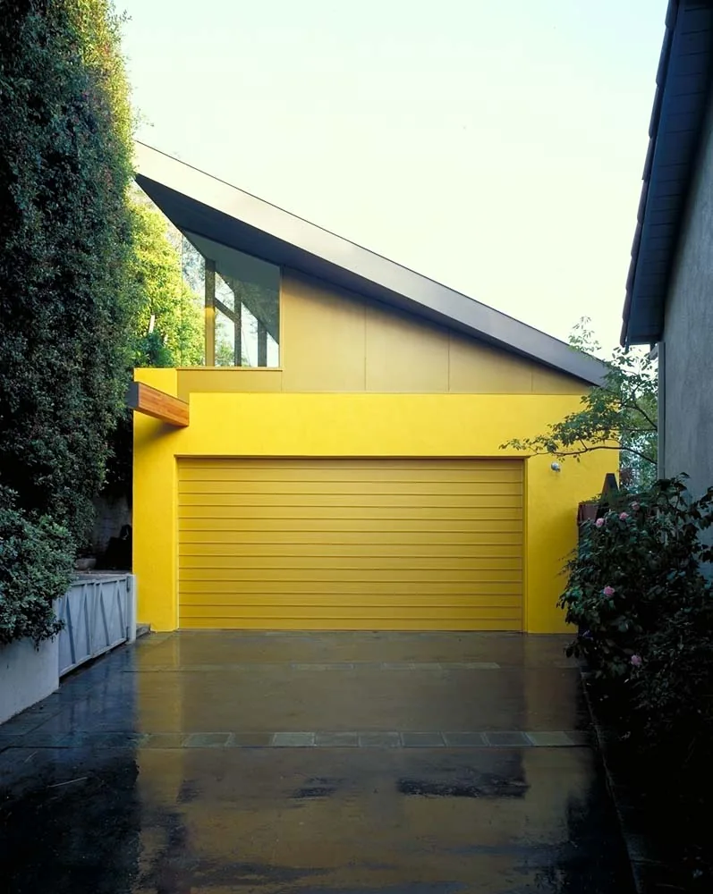 Exterior view of a yellow garage with a sloped roof and surrounding greenery.